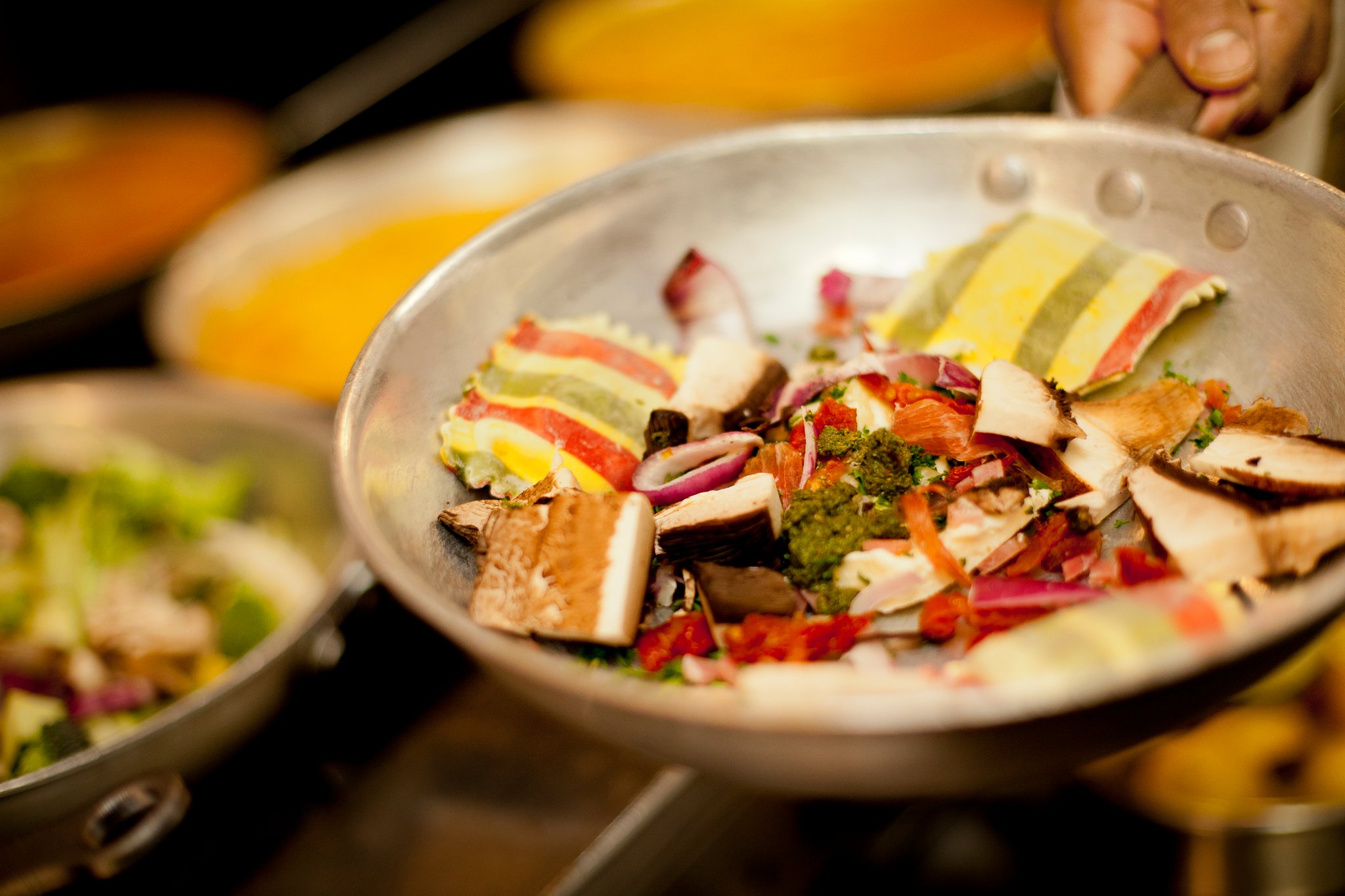 Person holding a metal plate with chopped vegetables and meat, with other dishes in the background.