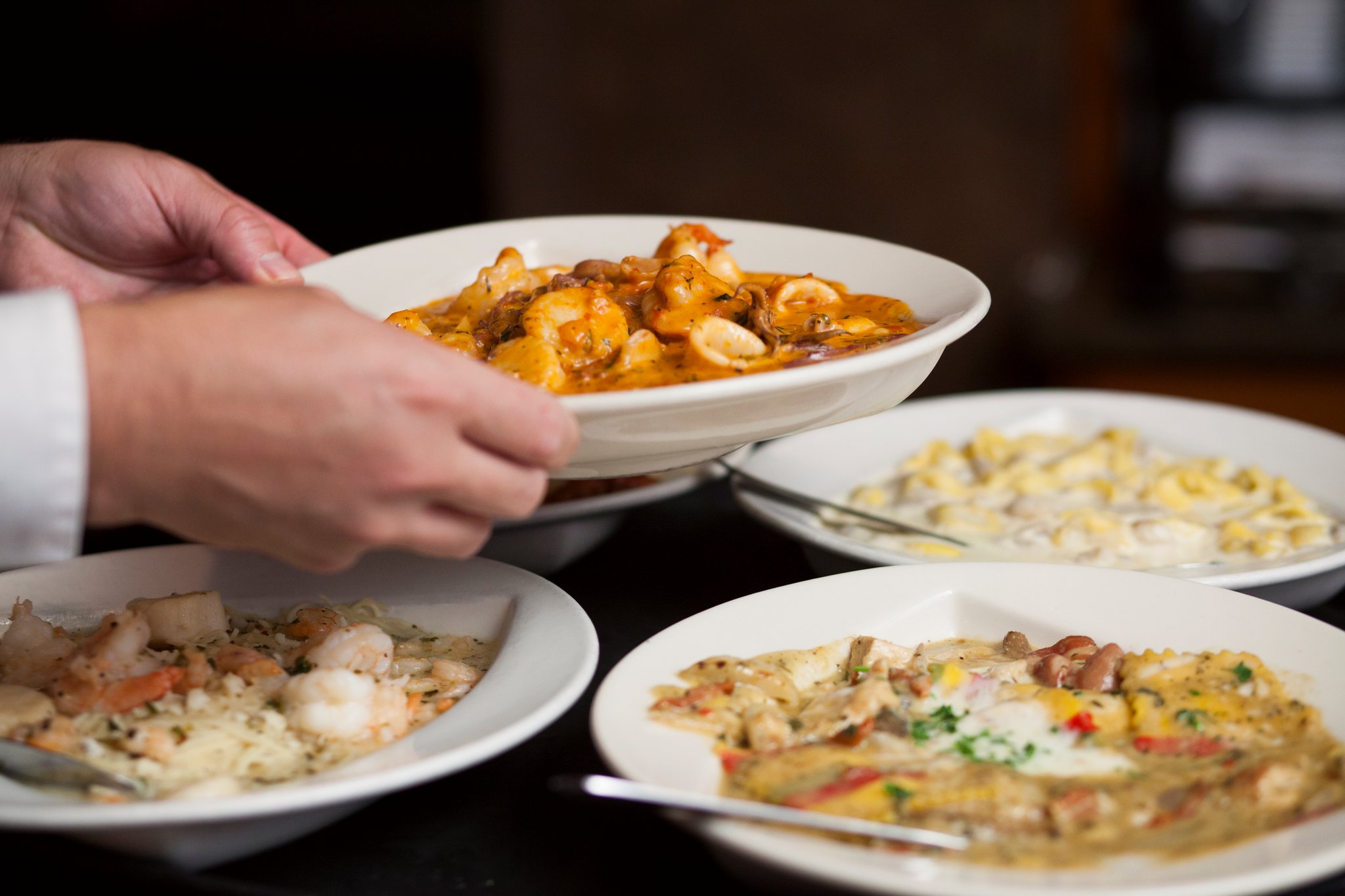 Person holding a bowl of pasta with sauce, with other dishes on the table.