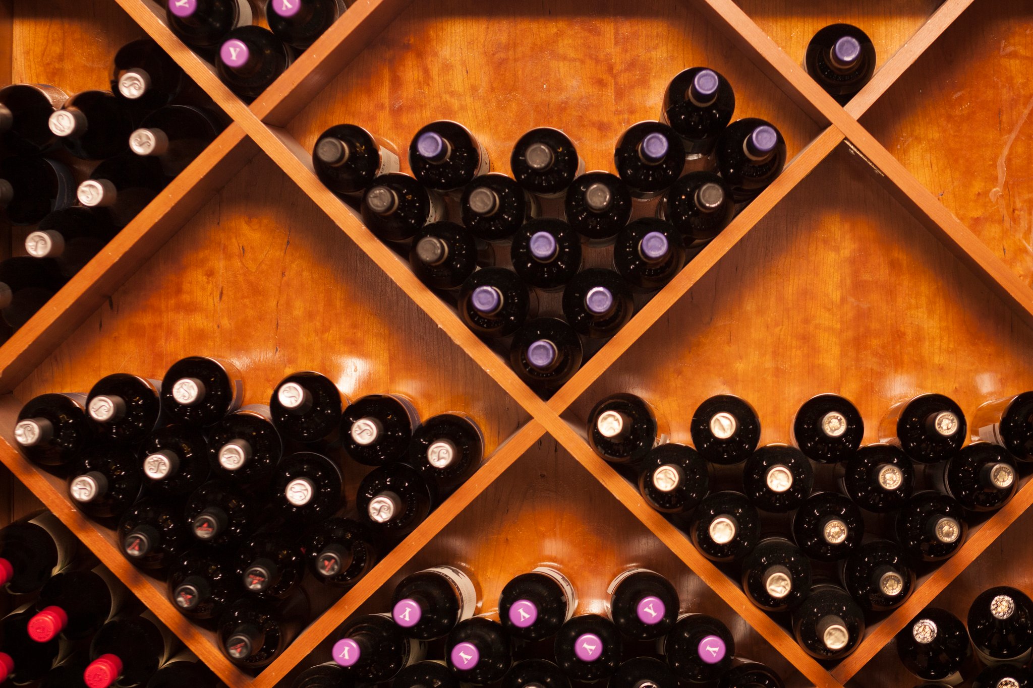 Wine bottles stored in wooden shelves arranged in diamond-shaped compartments.