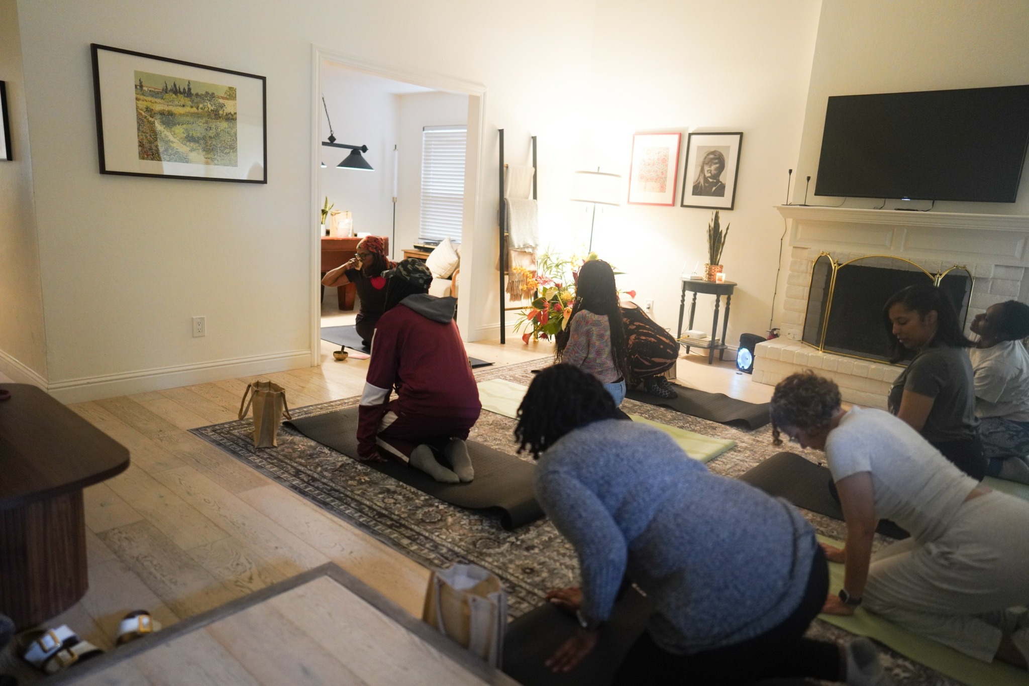 Group of people sitting on a rug in a living room, engaging in a group activity or discussion.