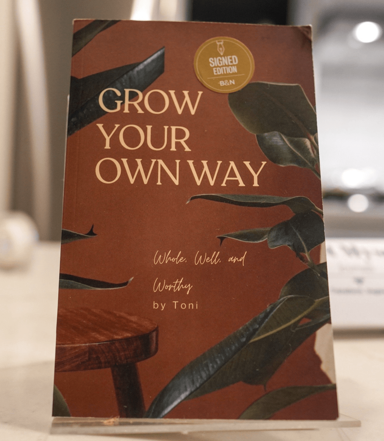 Book cover titled 'Grow Your Own Way' with leaves and a wooden surface, and a gold sticker at the top.