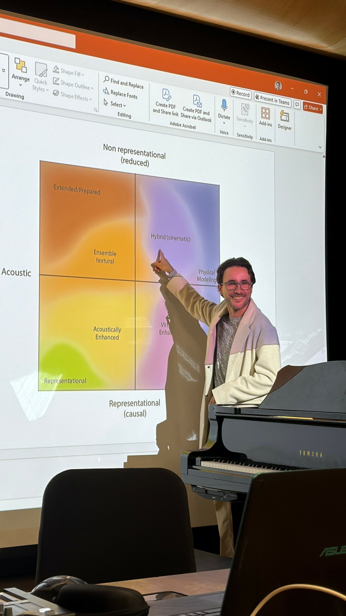 Person standing and pointing at a presentation slide projected on a screen, with a laptop and chairs in foreground.