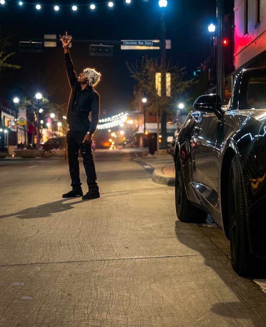 Person standing in the street at night, raising one arm with a cityscape and parked car nearby.