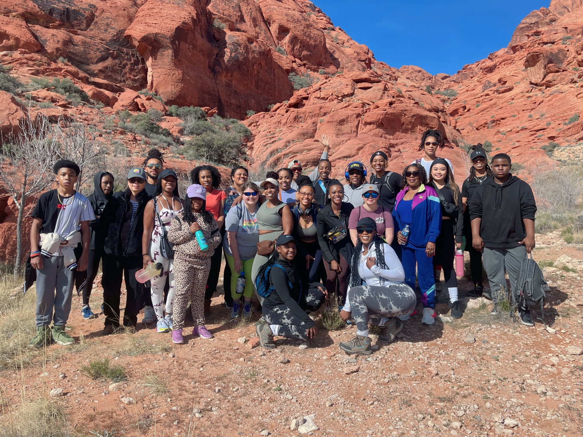 Group of people standing outdoors in a desert landscape with red rock formations and blue sky.