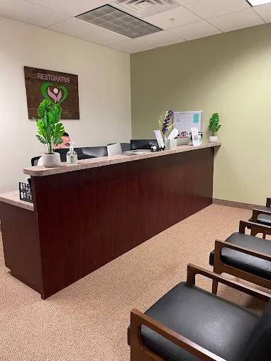 Reception desk with chairs in front, wall with a sign and plants behind the desk, and a light green wall.
