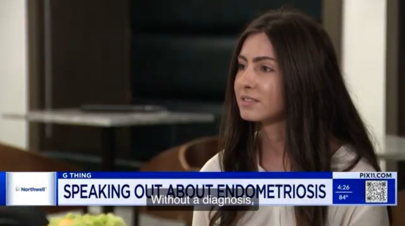 Woman with long dark hair speaking on television news program, background of a room with a desk and shelves.