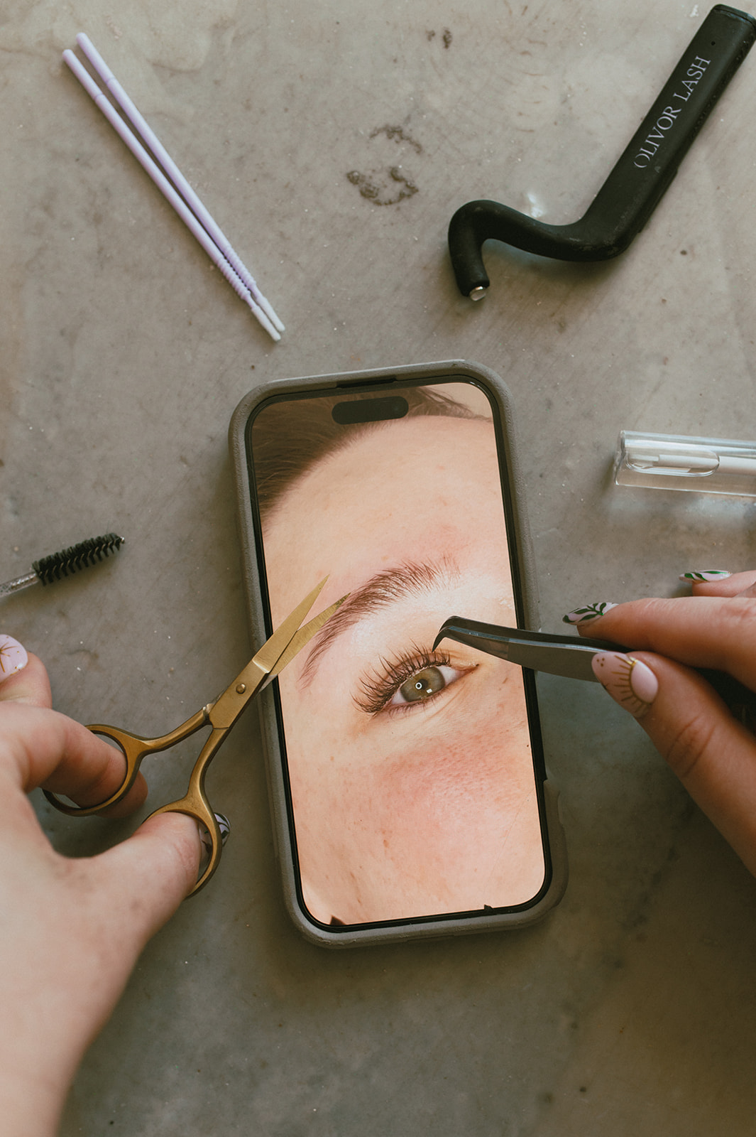 Close-up of a person using tweezers and a tool to work on an eye displayed on a smartphone screen, surrounded by tools.