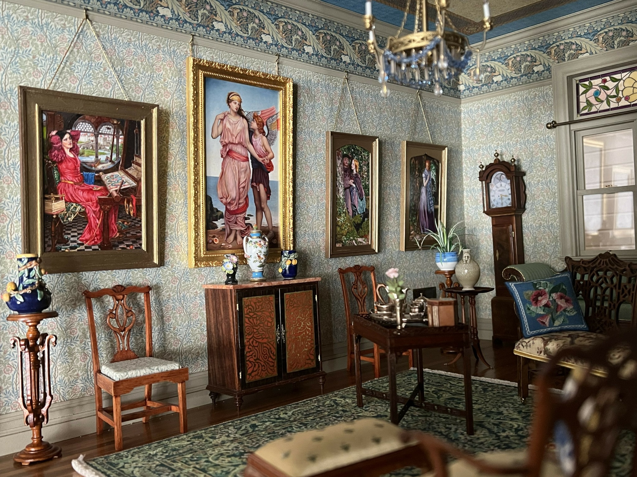 Elegant room with framed paintings, antique furniture, a chandelier, and decorative vases on side tables.