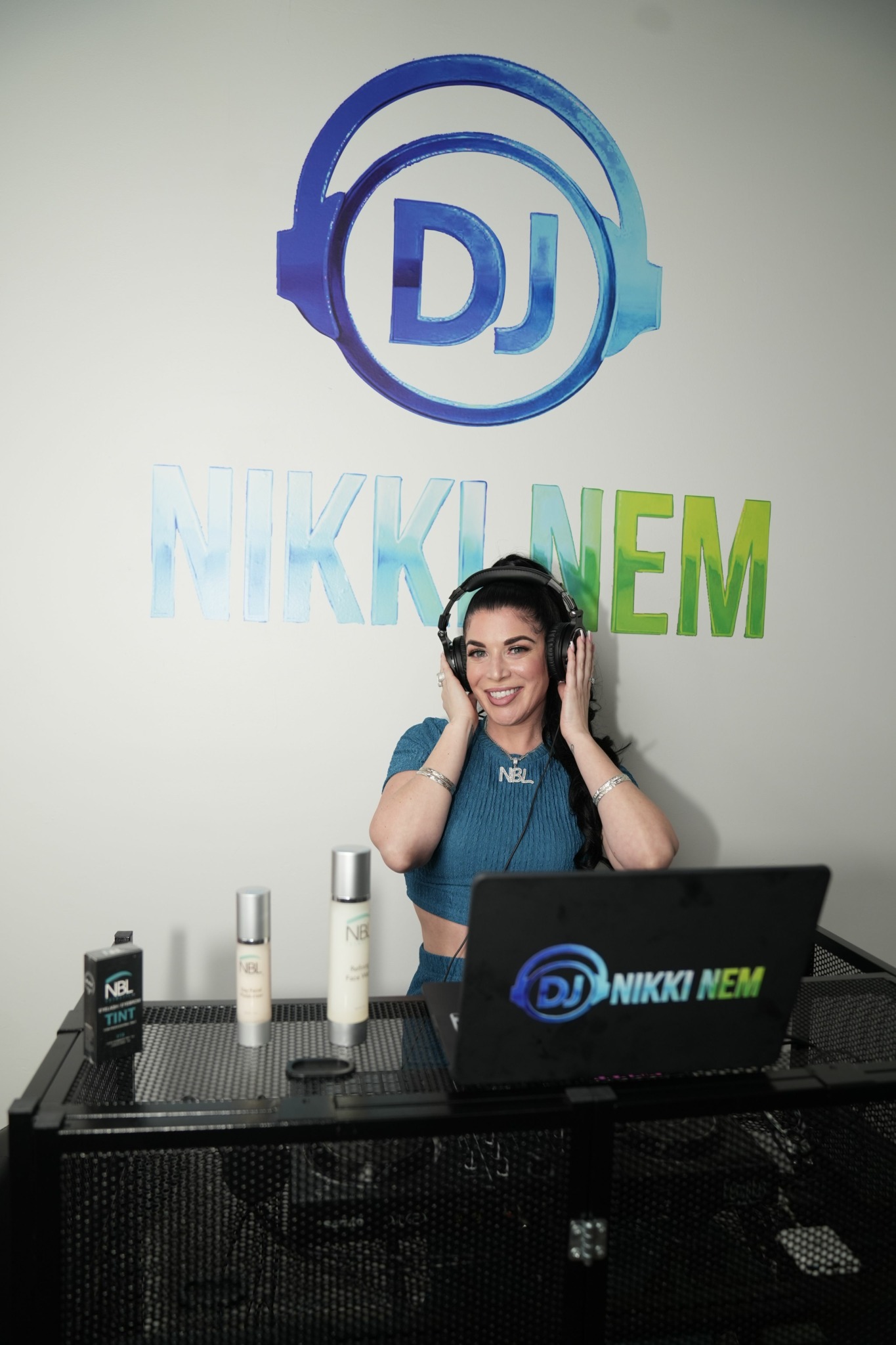 Woman with headphones sitting at DJ equipment in a studio with DJ logo and text on wall