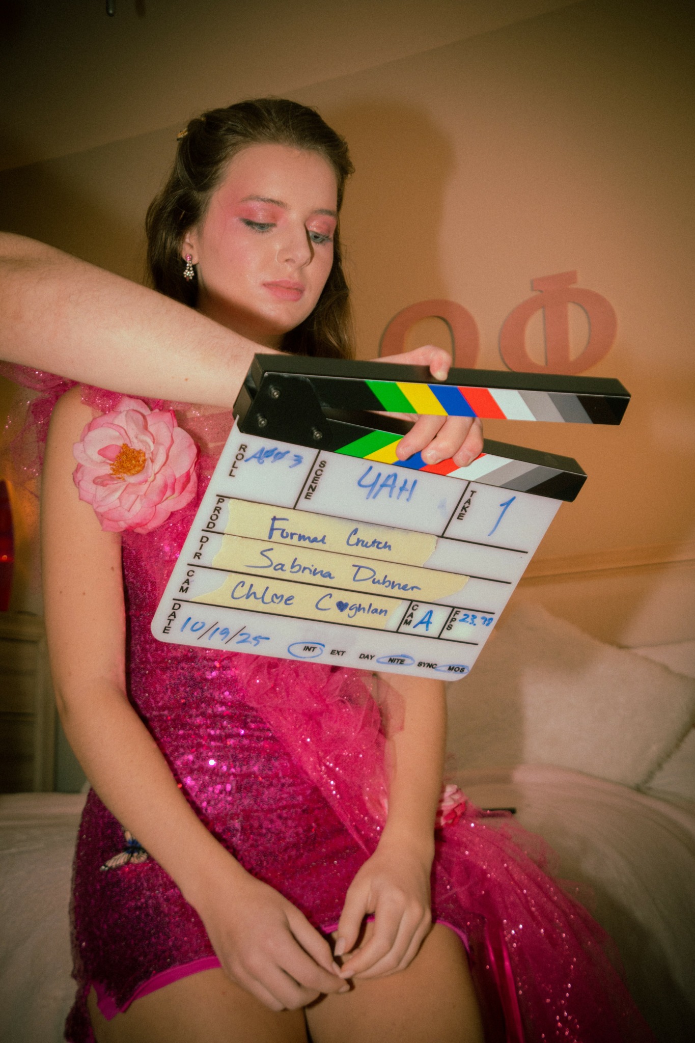 Young woman in pink dress with closed eyes, holding hands in front, behind a film slate, in a softly lit room.