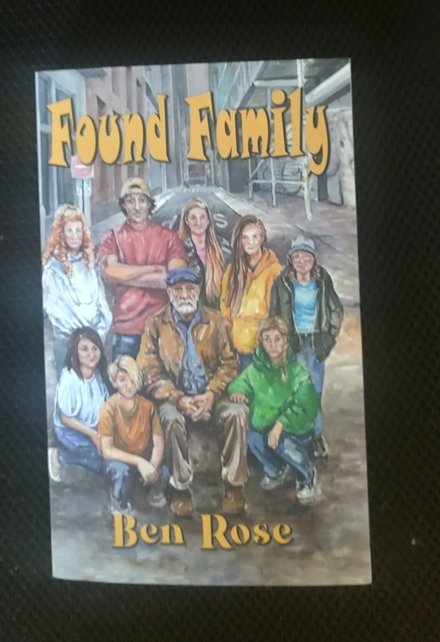 Book cover titled 'Found Family' by Ben Rose, featuring a group of diverse people outdoors with buildings in the background.