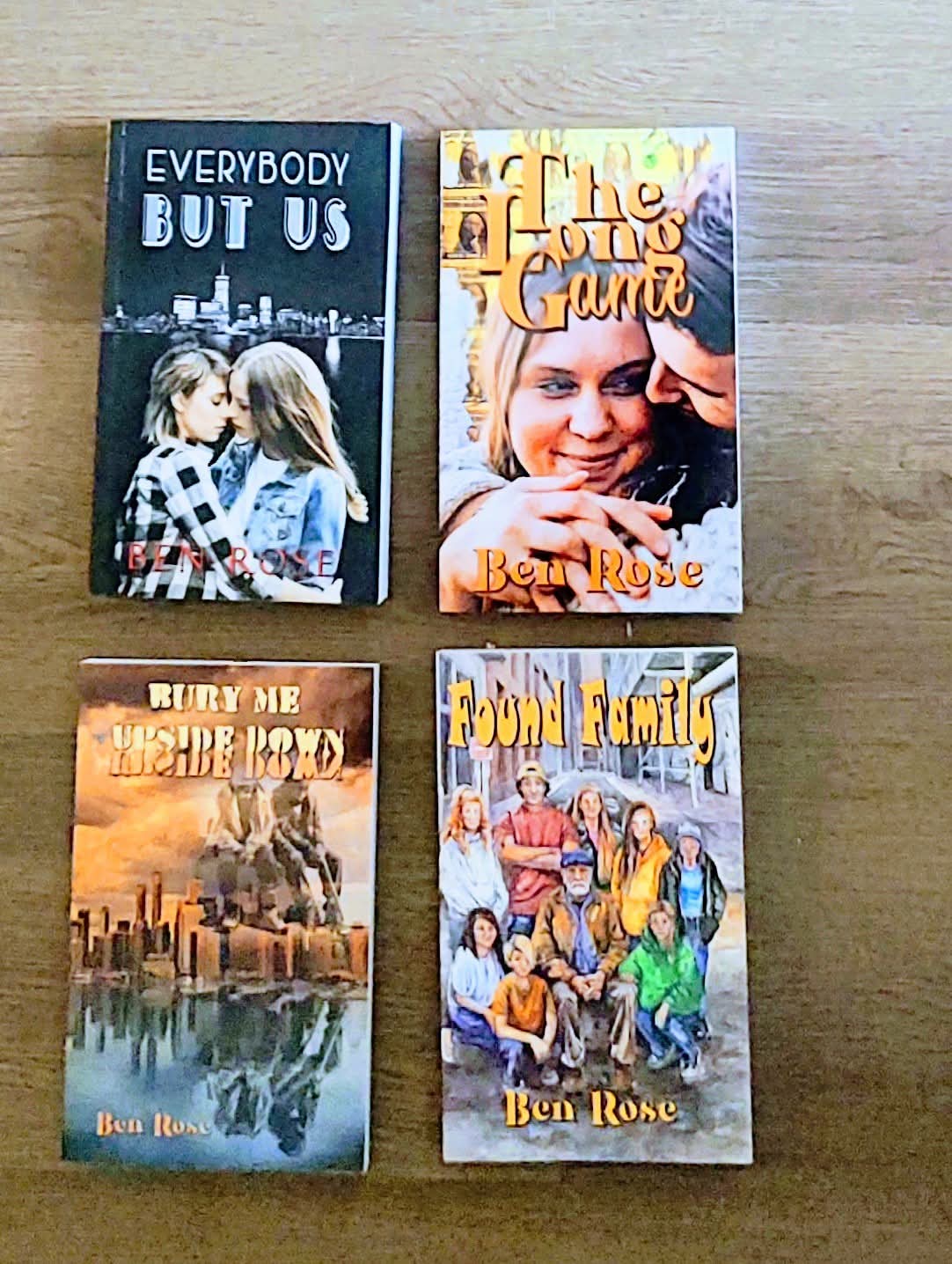 Four books arranged on a wooden surface, with titles visible, including 'Everybody But Us' and 'The Book of Family'.
