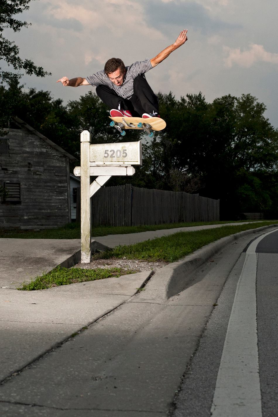 Boy skateboarding in mid-air above a mailbox, with trees and a cloudy sky in background.