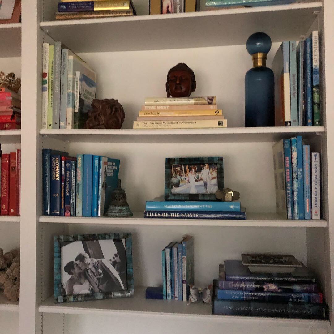 White bookshelf with books, decorative items, and photographs arranged on four shelves.