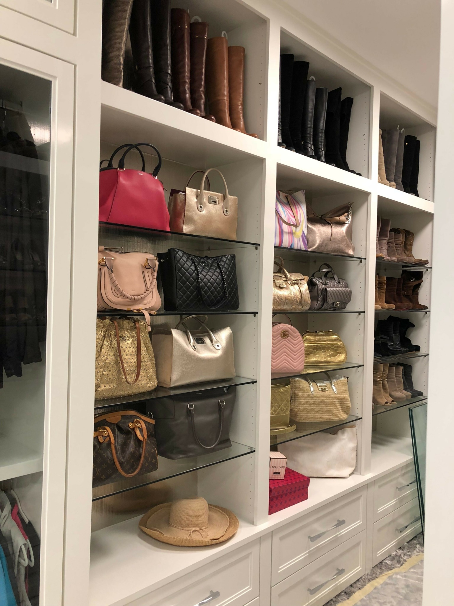 Open closet with shelves containing shoes and handbags, viewed from the side, with a drawer and a round object nearby.