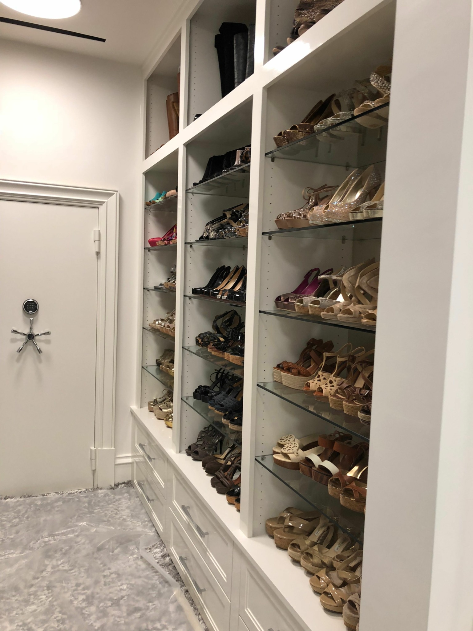 Shoes stored in cubbies on a white shelf, viewed from the side, with a gray floor and white wall.