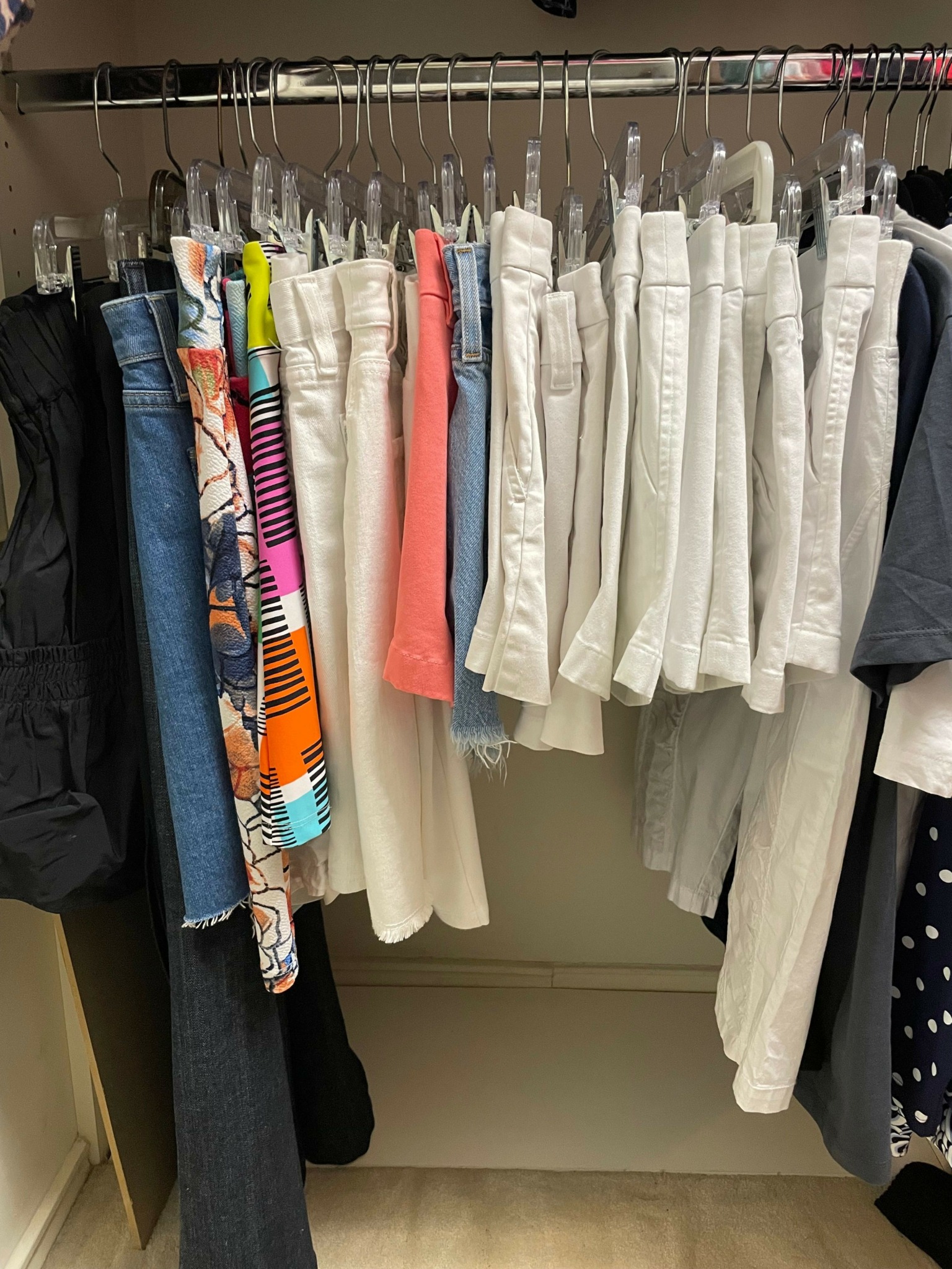 Clothes hanging on a rack, mostly white, with some colorful and darker items, in a retail or storage setting.