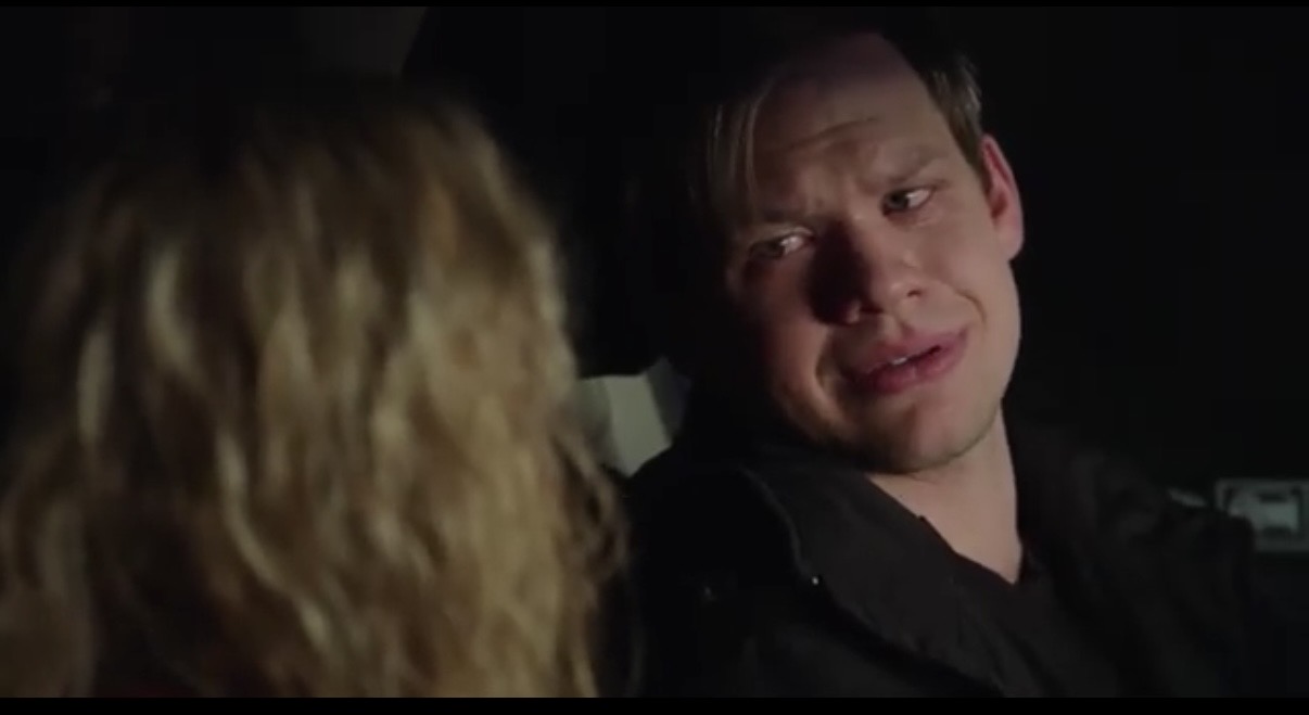 A man and a woman are in a car at night, with the man looking at the woman with a concerned expression.
