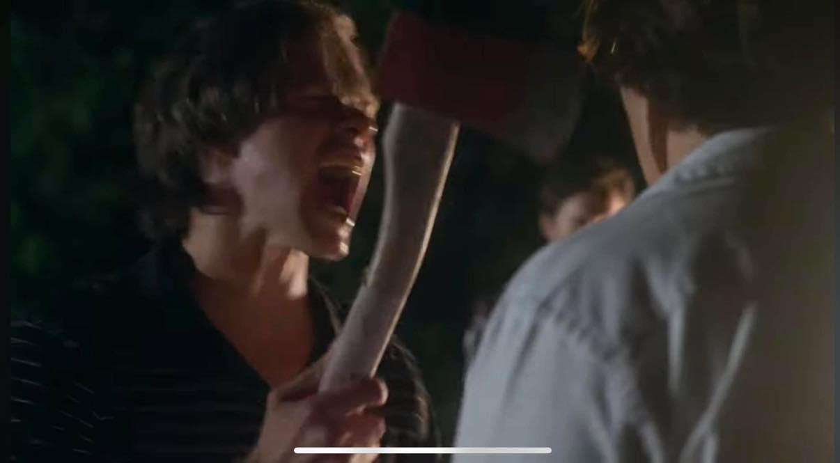 Person shouting at another person holding an axe, nighttime outdoor scene, intense confrontation, dark background