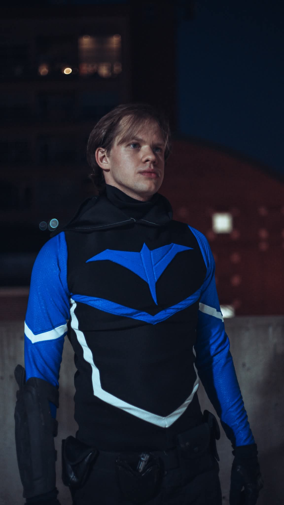Young person with short hair wearing a blue and black jacket, standing outdoors at night.