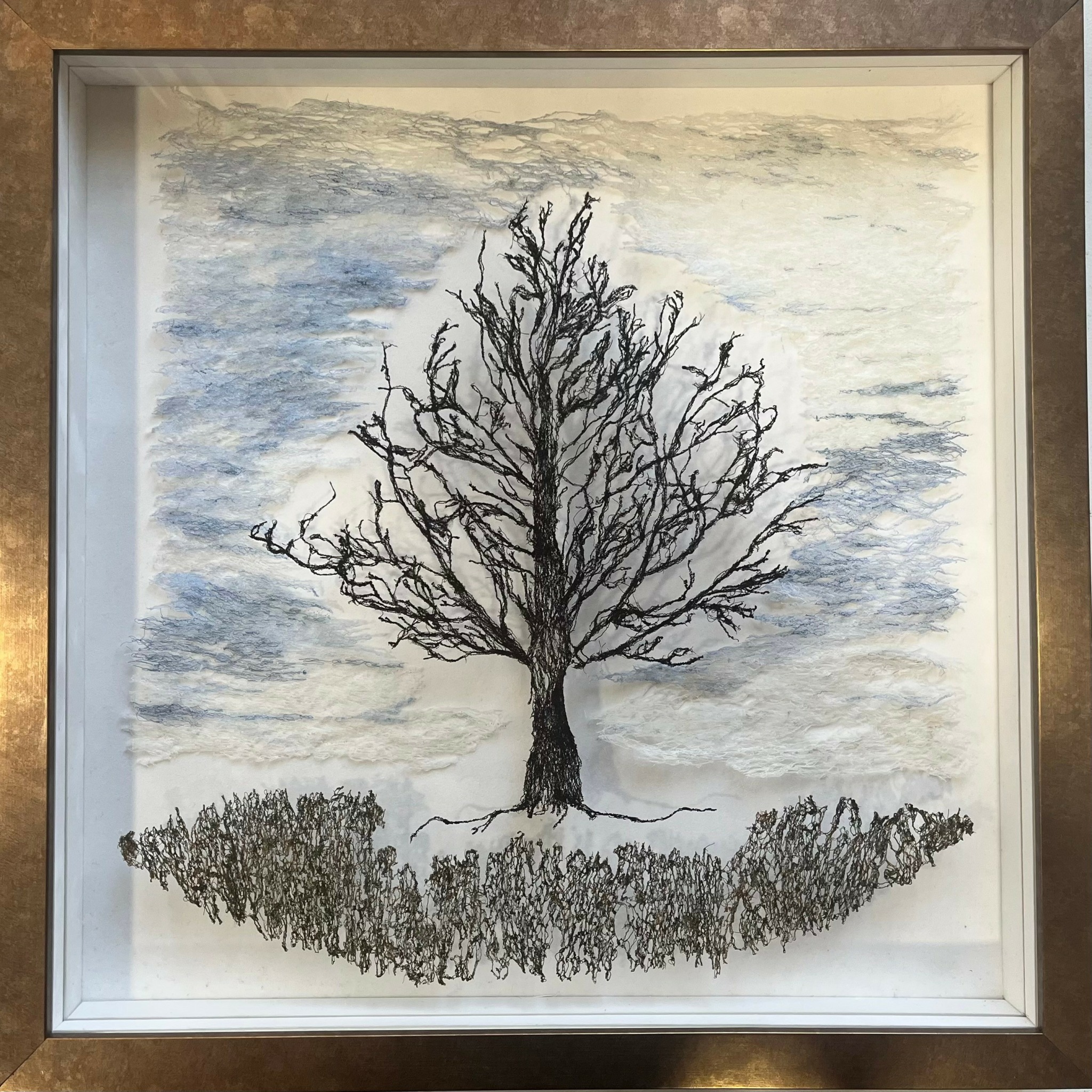 A leafless tree with a wide canopy stands on a grassy patch against a cloudy sky.