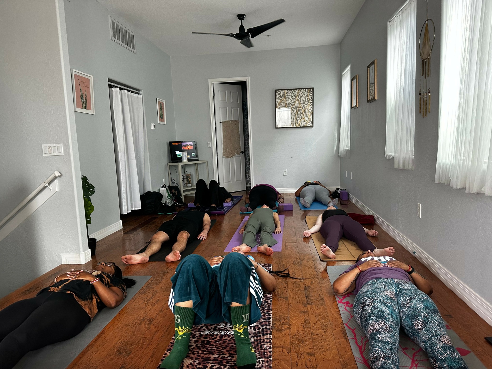 People lying on yoga mats and blankets in a bright room with windows, practicing relaxation or meditation.
