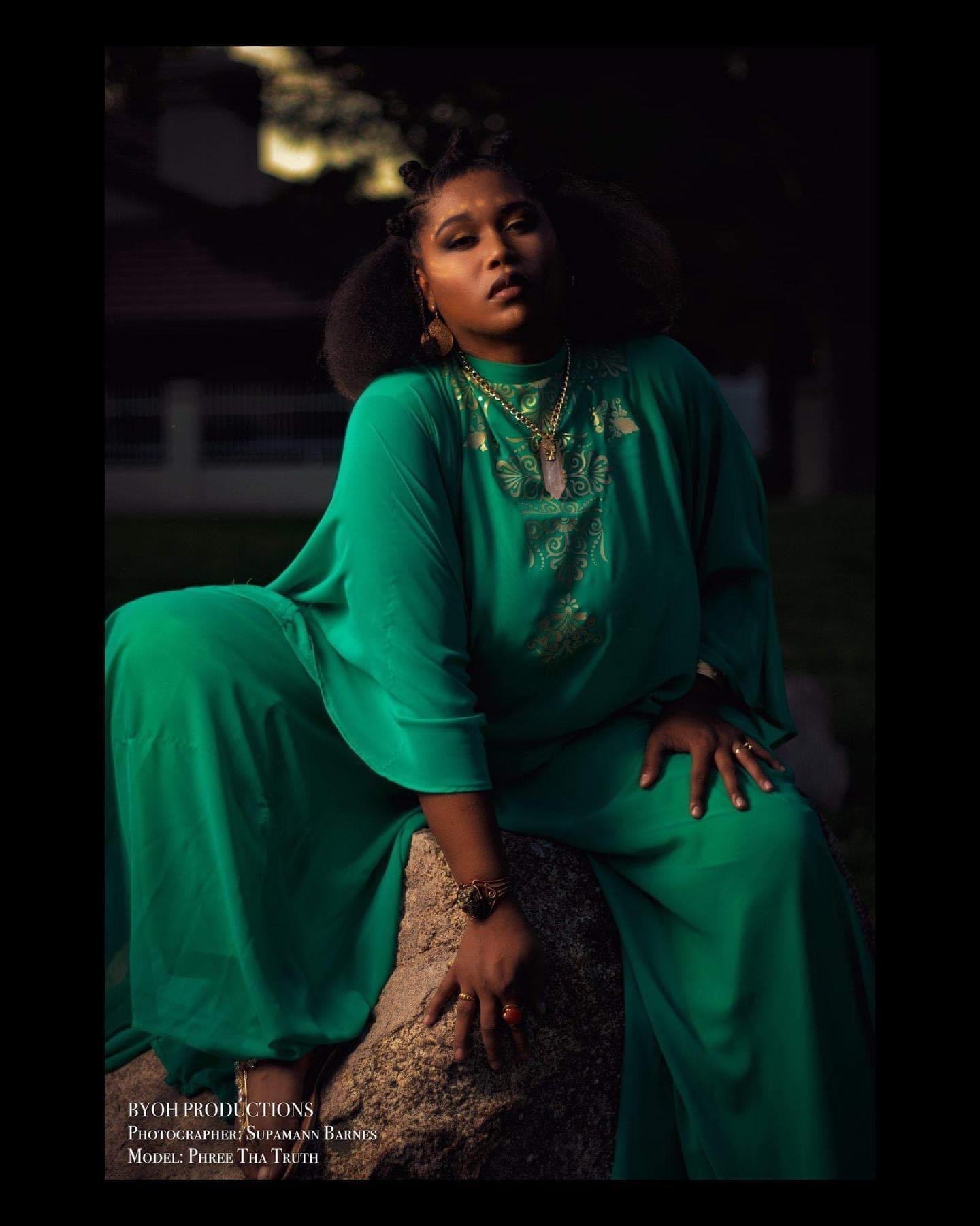 Woman in green dress sitting outdoors at night, dark background, confident expression, large hairstyle, jewelry, and accessories.
