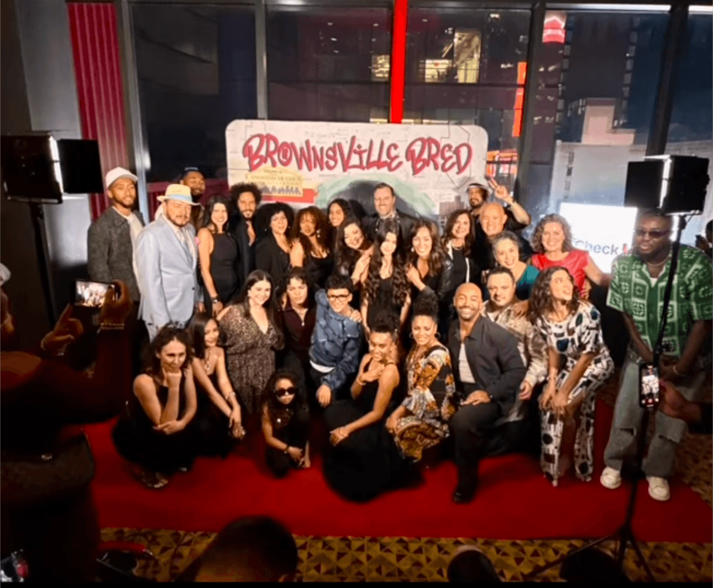 Group of people posing in front of a sign that reads 'Brownsville Red' at an indoor event, some holding drinks.