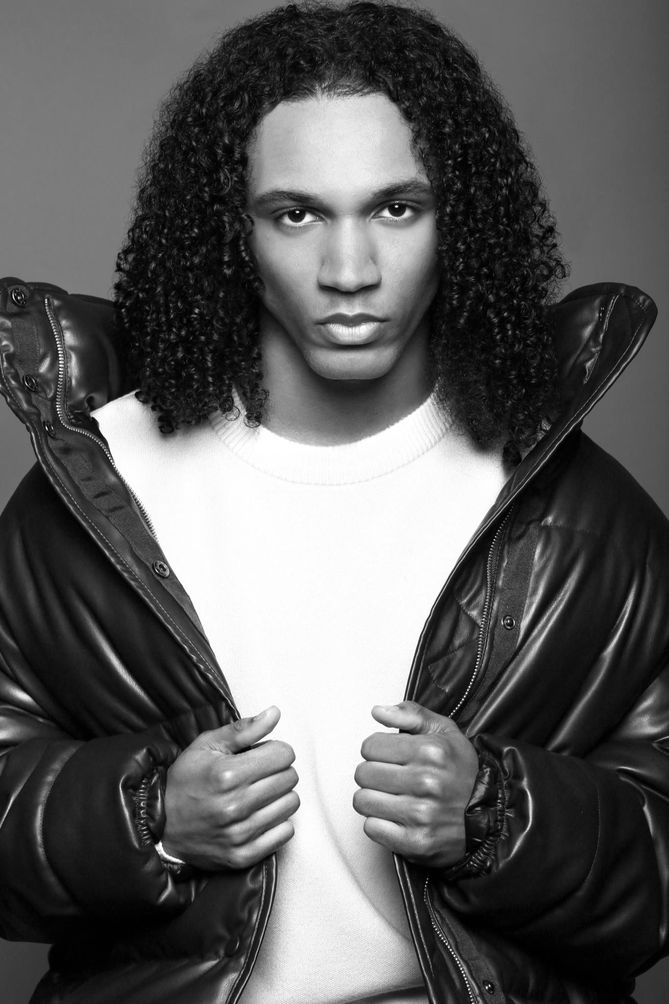 Black and white portrait of a person with curly hair wearing a jacket and white shirt, looking directly at the camera.