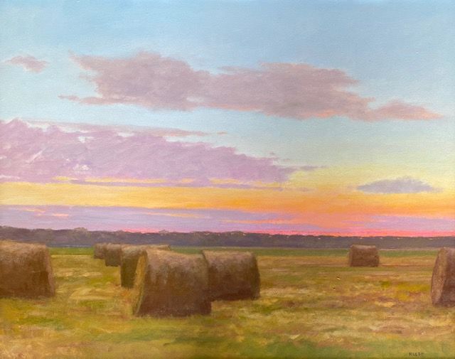 Sunset sky with pink and orange clouds over a field with hay bales, landscape scene.