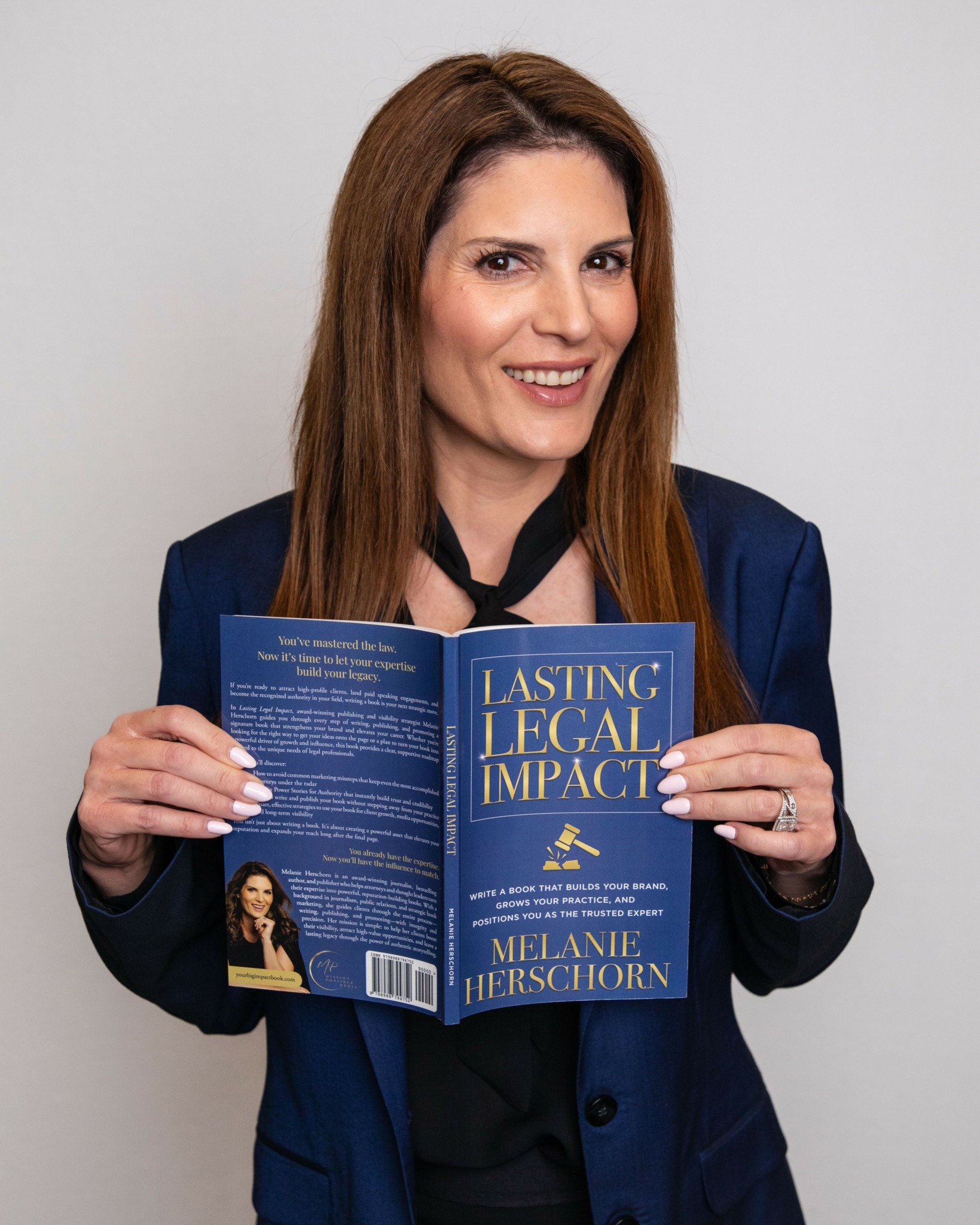Woman with long brown hair holding a blue book titled 'Lasting Legal Impact' by Melanie Hershorn, smiling, against a plain background.