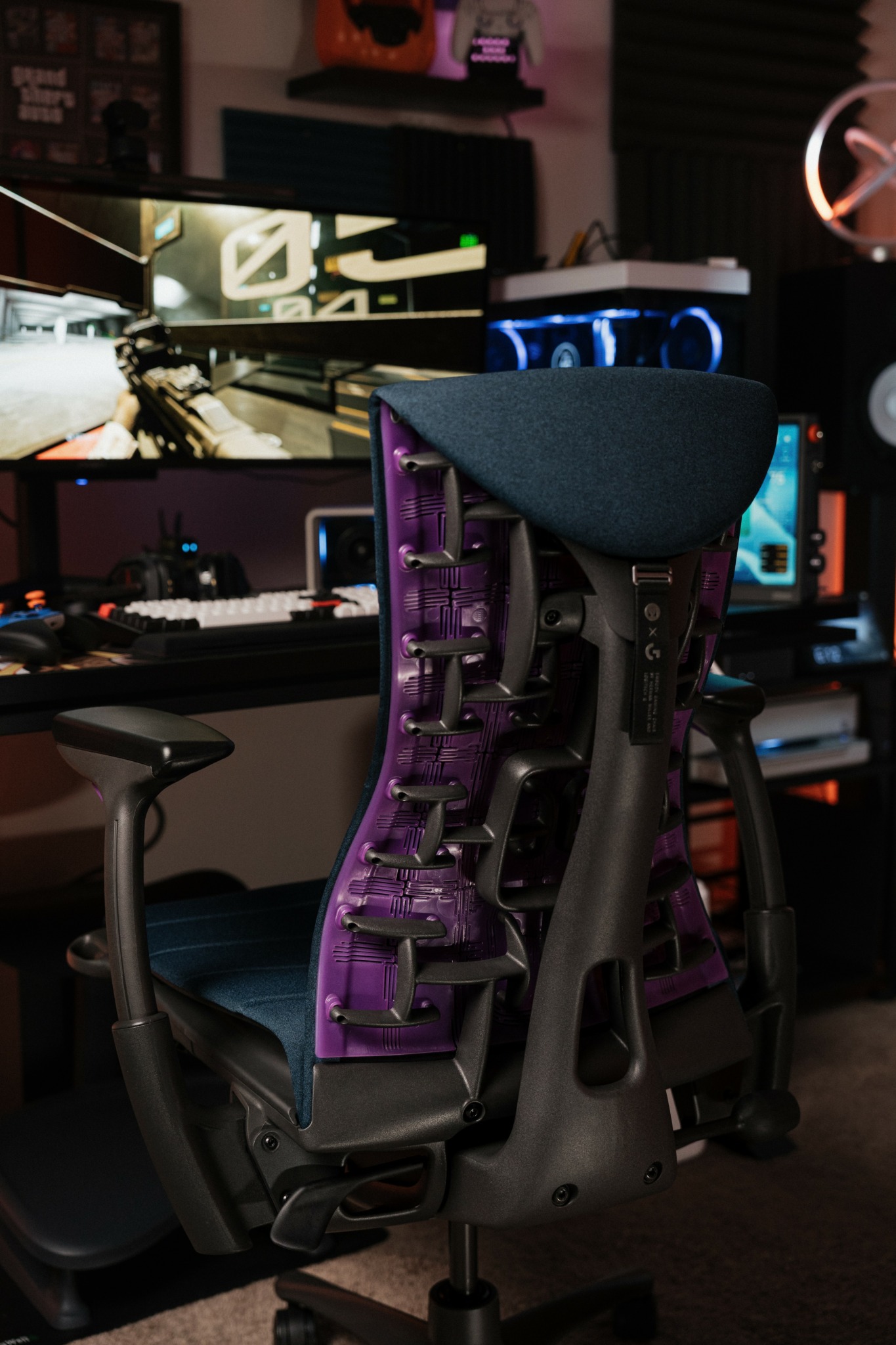 Office workspace with a gaming chair, computer monitors, and audio equipment in a dimly lit room.
