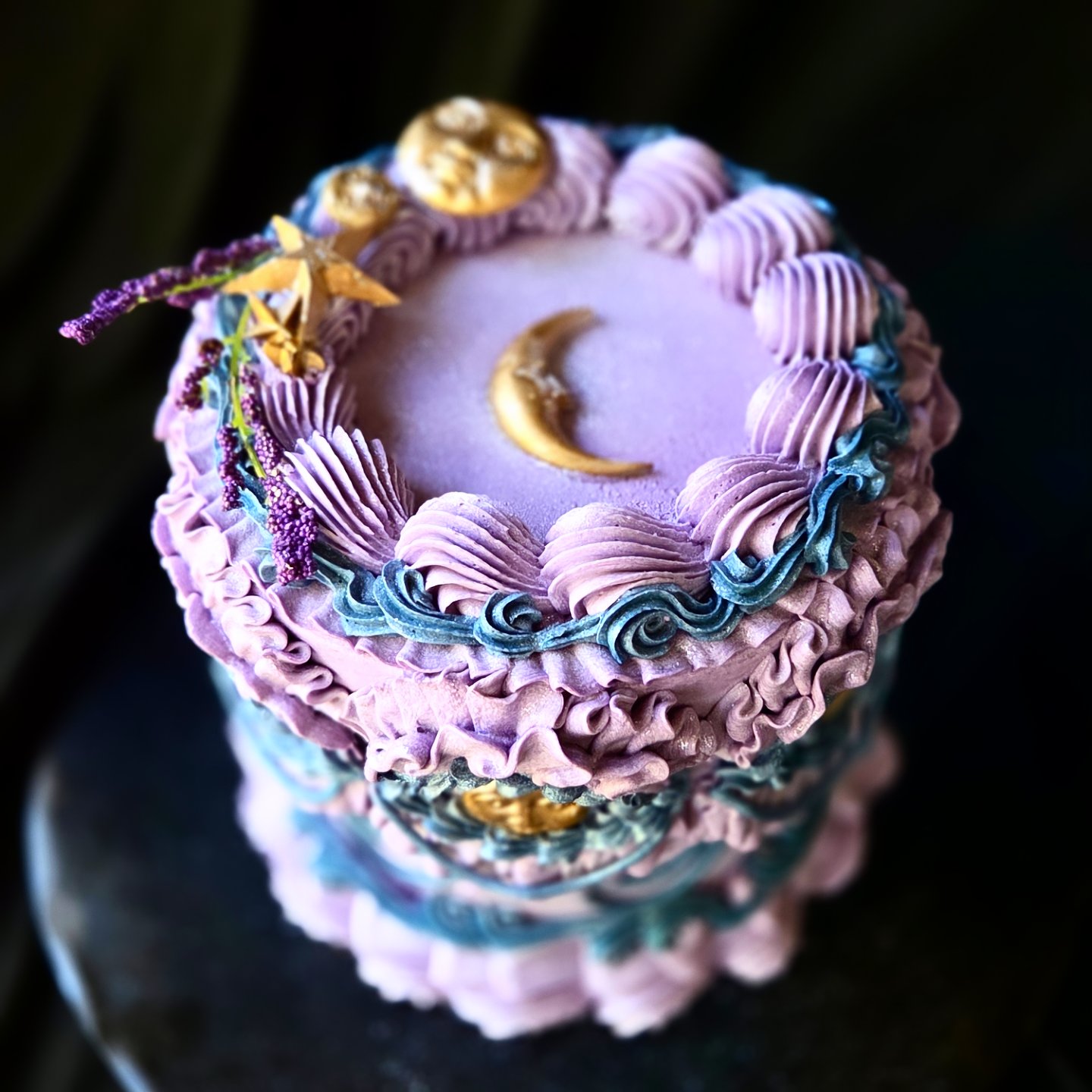 Decorative cake with purple, blue, and gold accents, featuring a crescent moon and floral decorations, viewed from above.