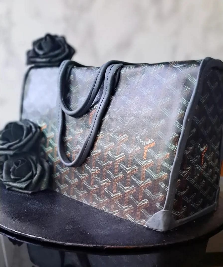 A patterned bag with black handles and a black base, placed on a surface with fabric flowers nearby.