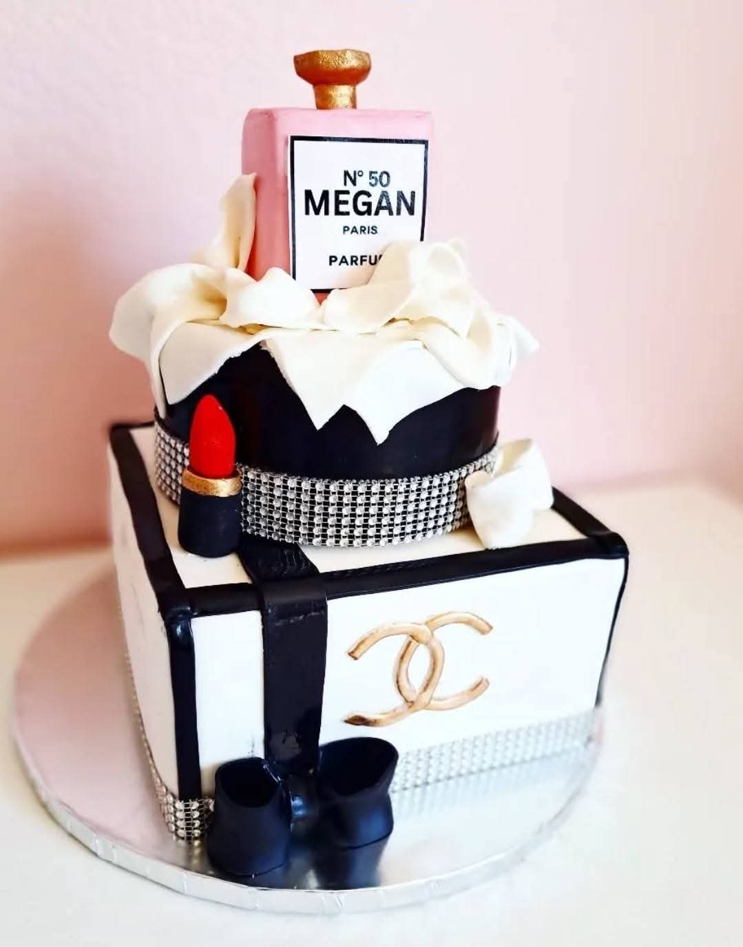 Cake designed as a luxury handbag with lipstick, perfume, and accessories, decorated with rhinestones and a bow, on a round base.
