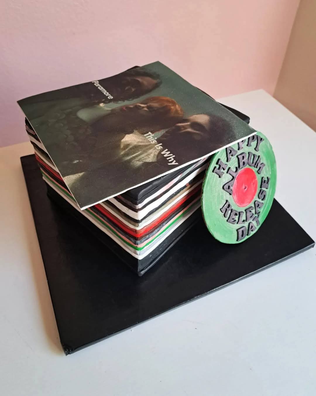 Stack of vinyl records and a CD on a black folder, with a pink wall in the background.