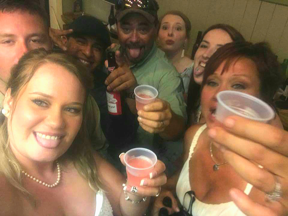 Group of people smiling and holding drinks at a social gathering, some making gestures, in an indoor setting.