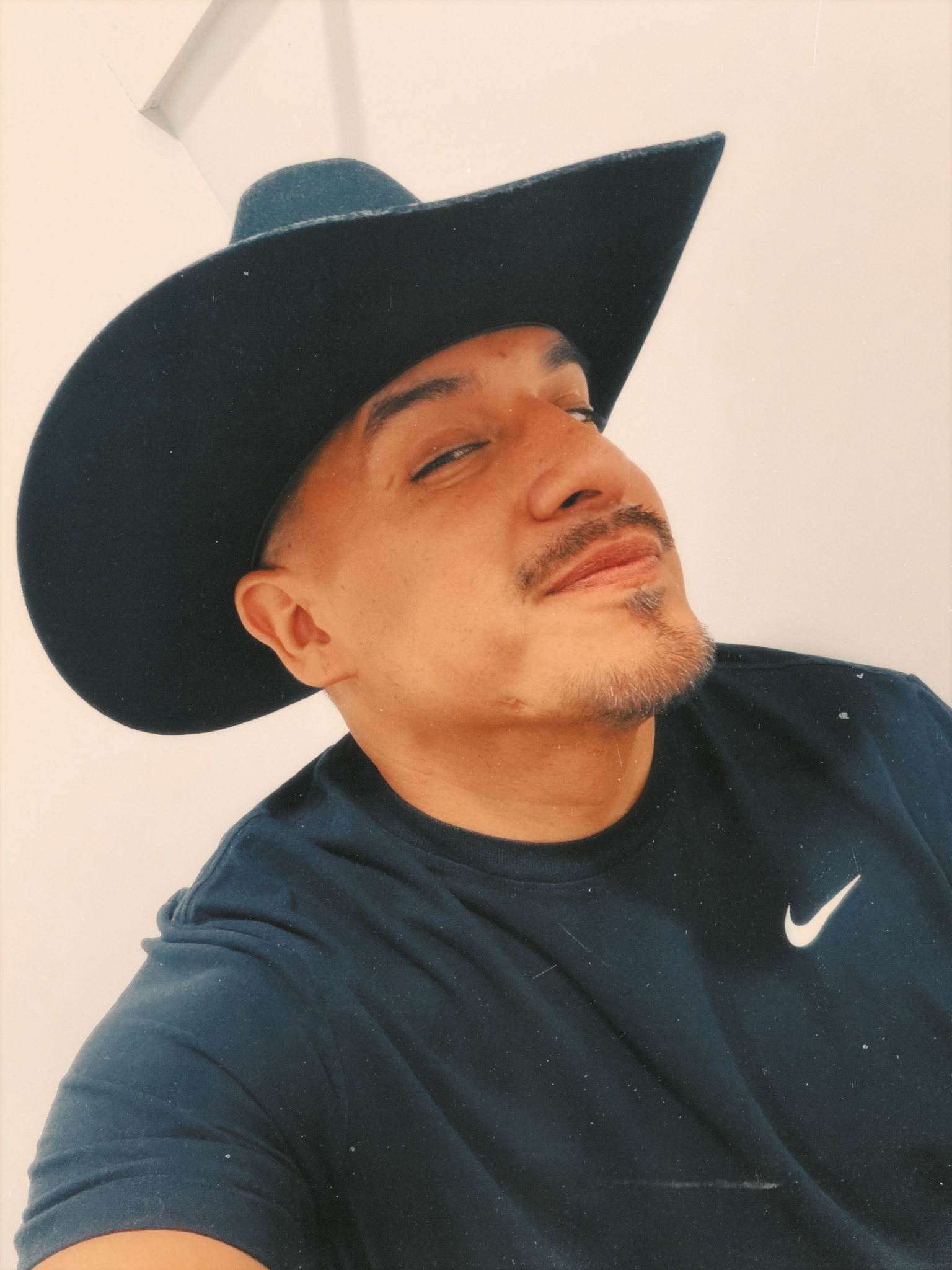 Man wearing a large black hat and black Nike shirt, looking sideways with a slight smile.