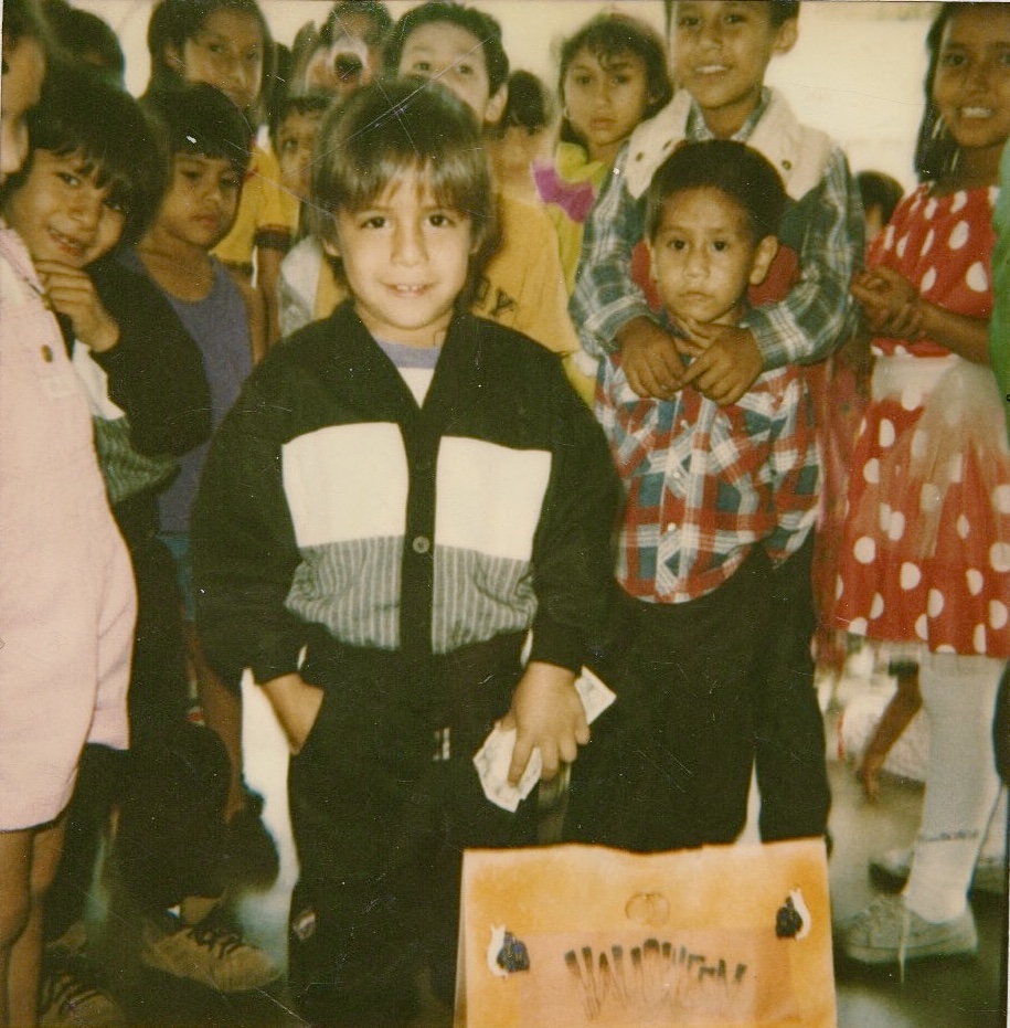 Group of children, with a girl in the center wearing a black and white jacket, standing in a classroom.