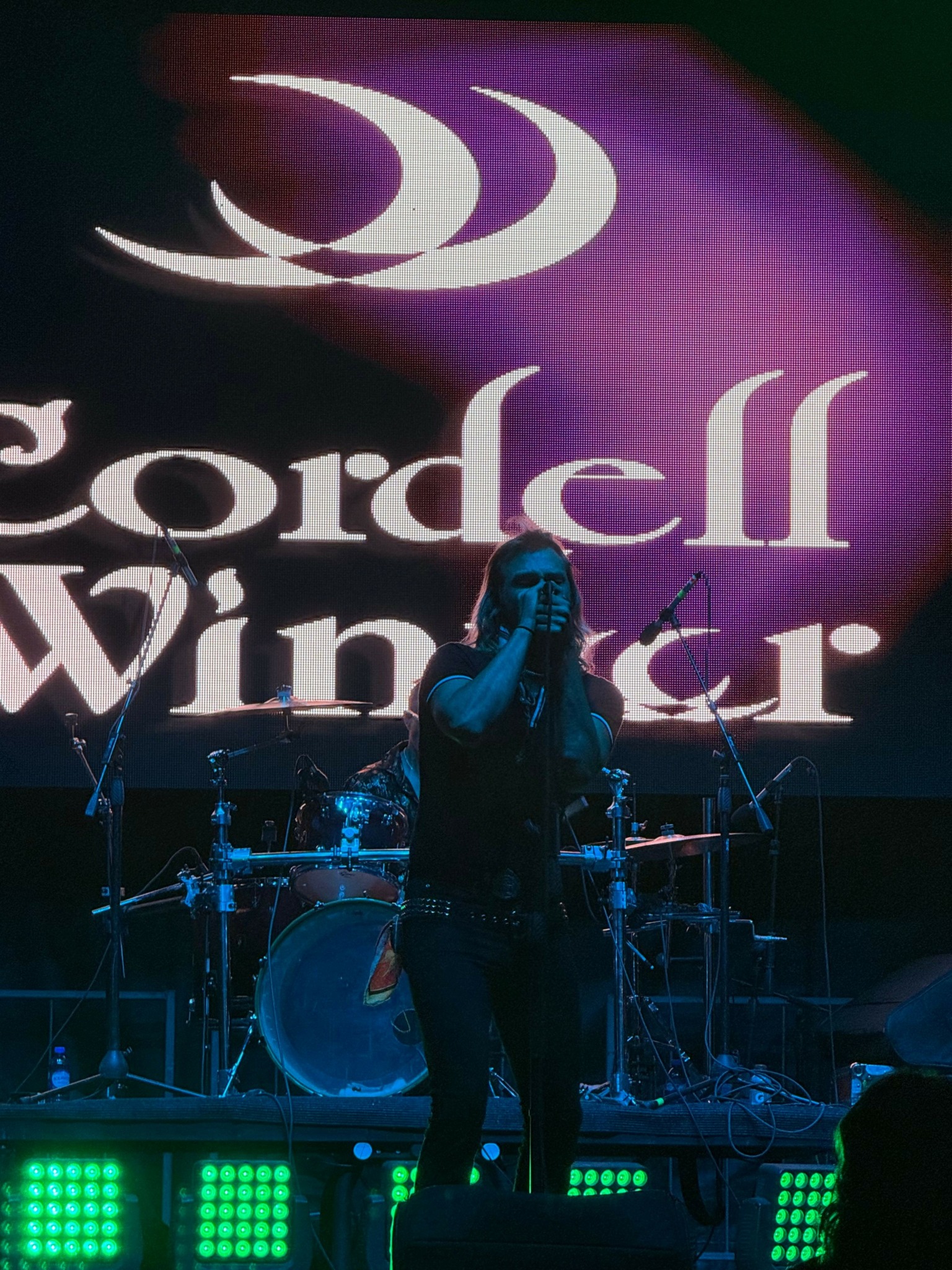 Person speaking on stage with a large screen displaying 'World' and 'Ch' behind them, stage lights visible.