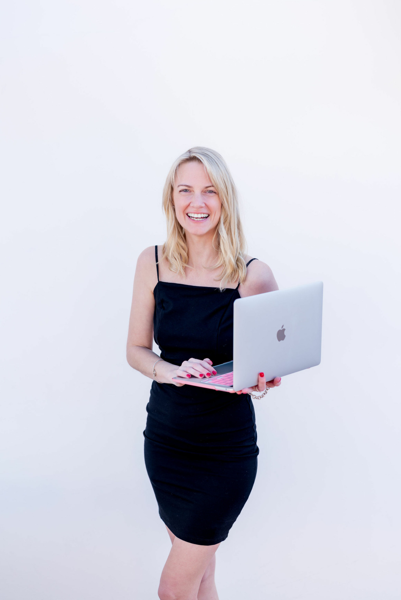 Smiling woman holding a laptop, standing against a plain white background.
