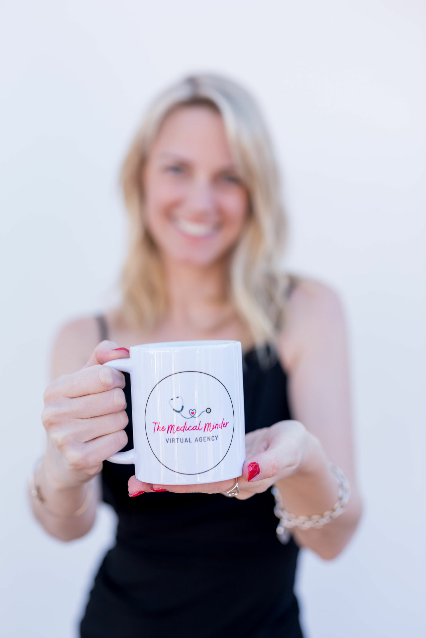 Blurry woman smiling and holding a white mug with a smiley face and text, against a plain background.