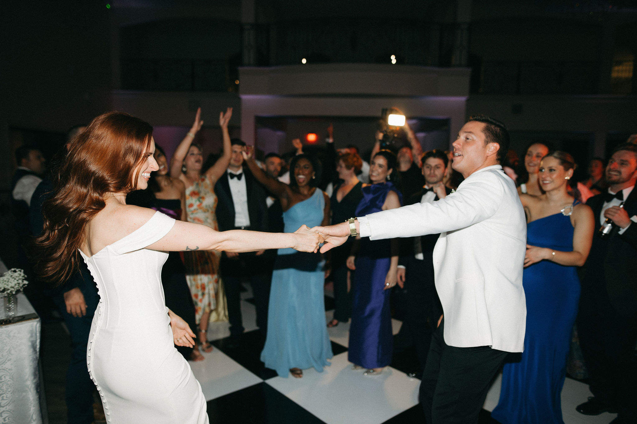 Couple dancing and holding hands at a formal event with a crowd in the background.