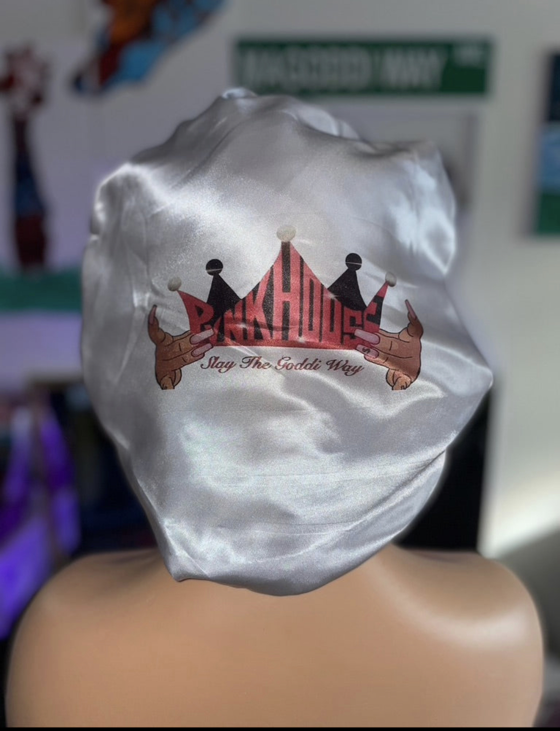 Silky fabric with a logo featuring a pink crown, black figures, and text, draped over a mannequin's head.