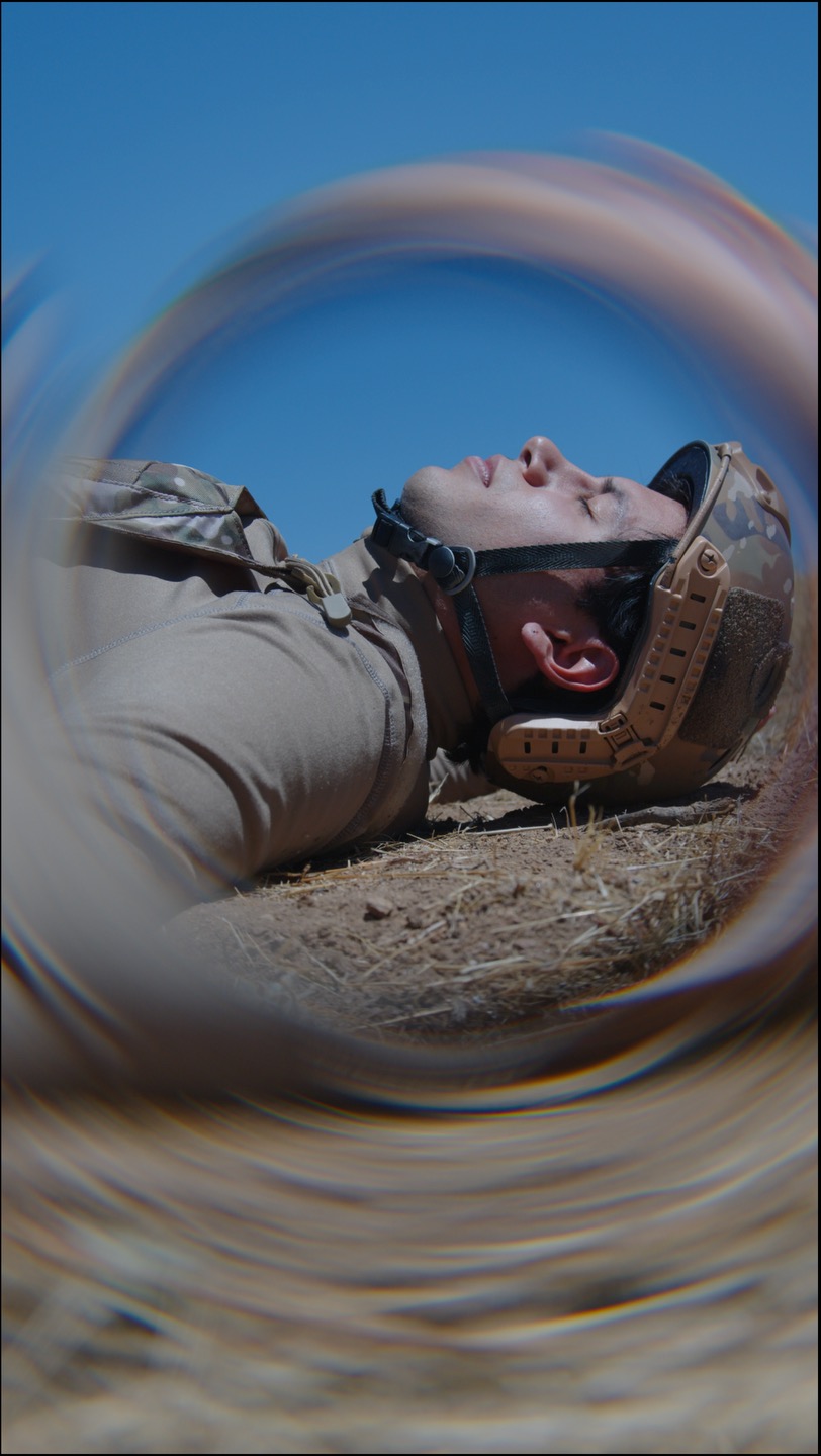 Person lying on ground with helmet, viewed through a circular frame, with blue sky background.
