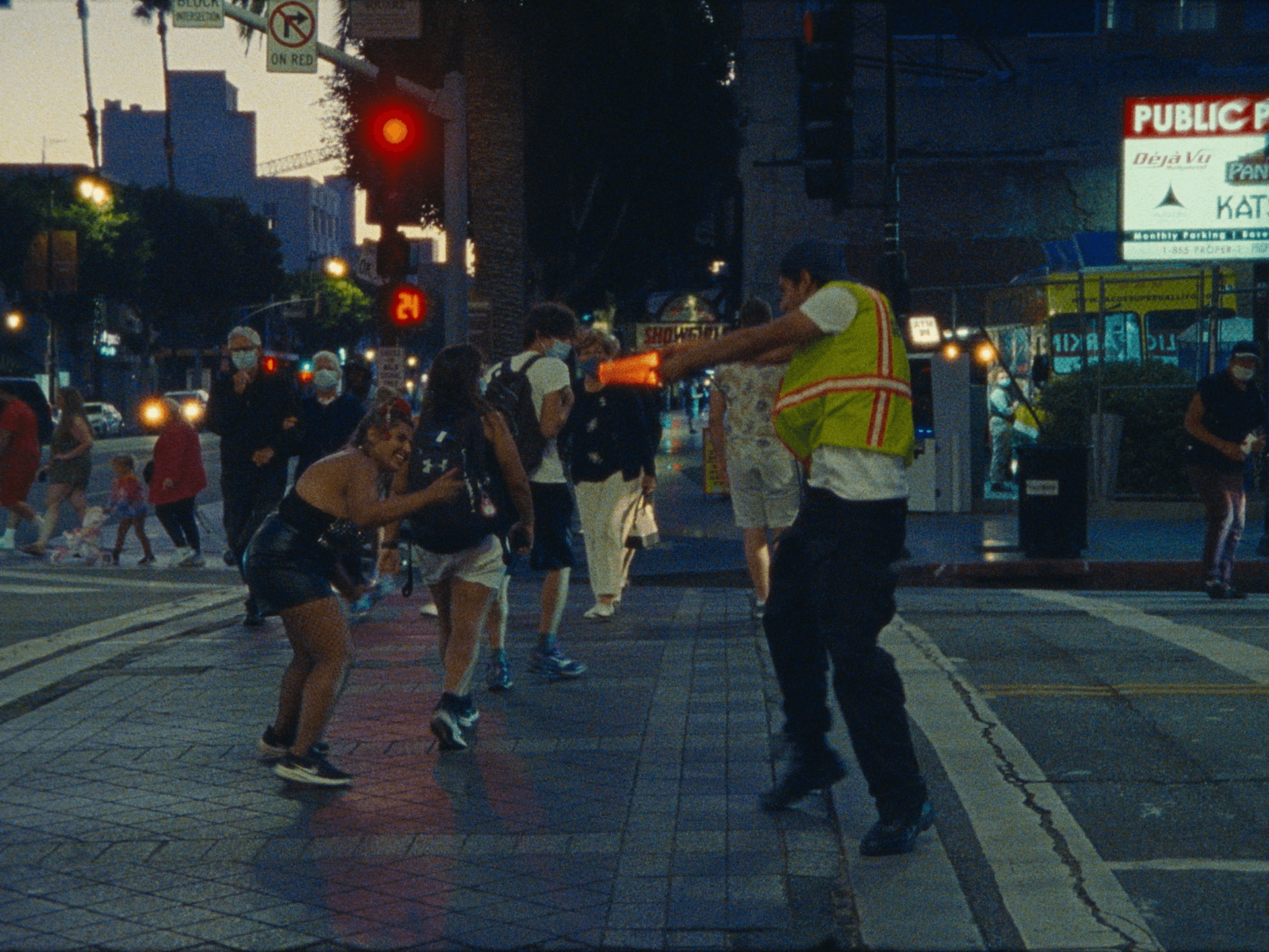 Traffic officer directing pedestrians at a city crosswalk during evening, with people walking and traffic lights visible.