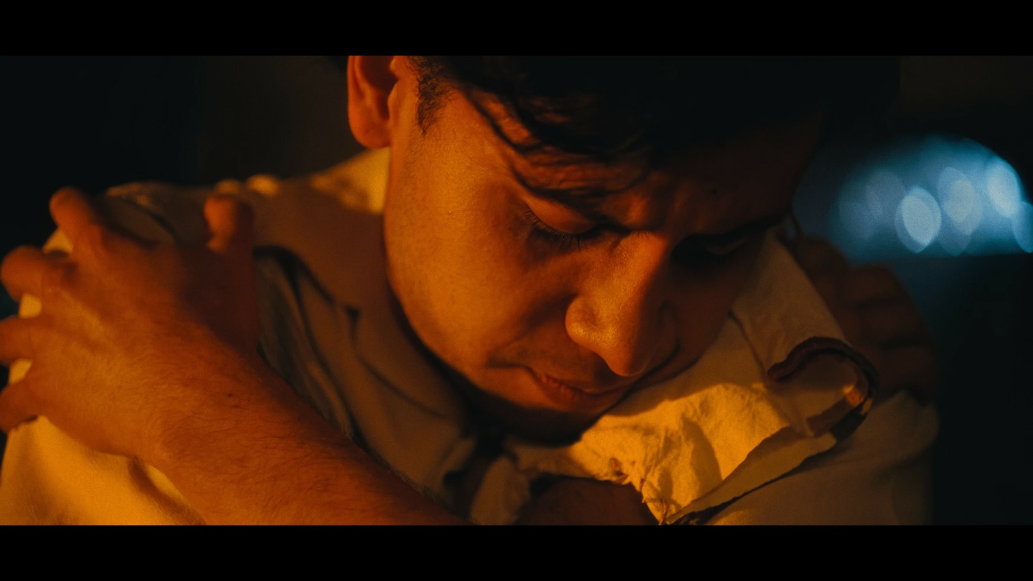 Close-up of a person with eyes closed, resting their head on their arm, in warm lighting.