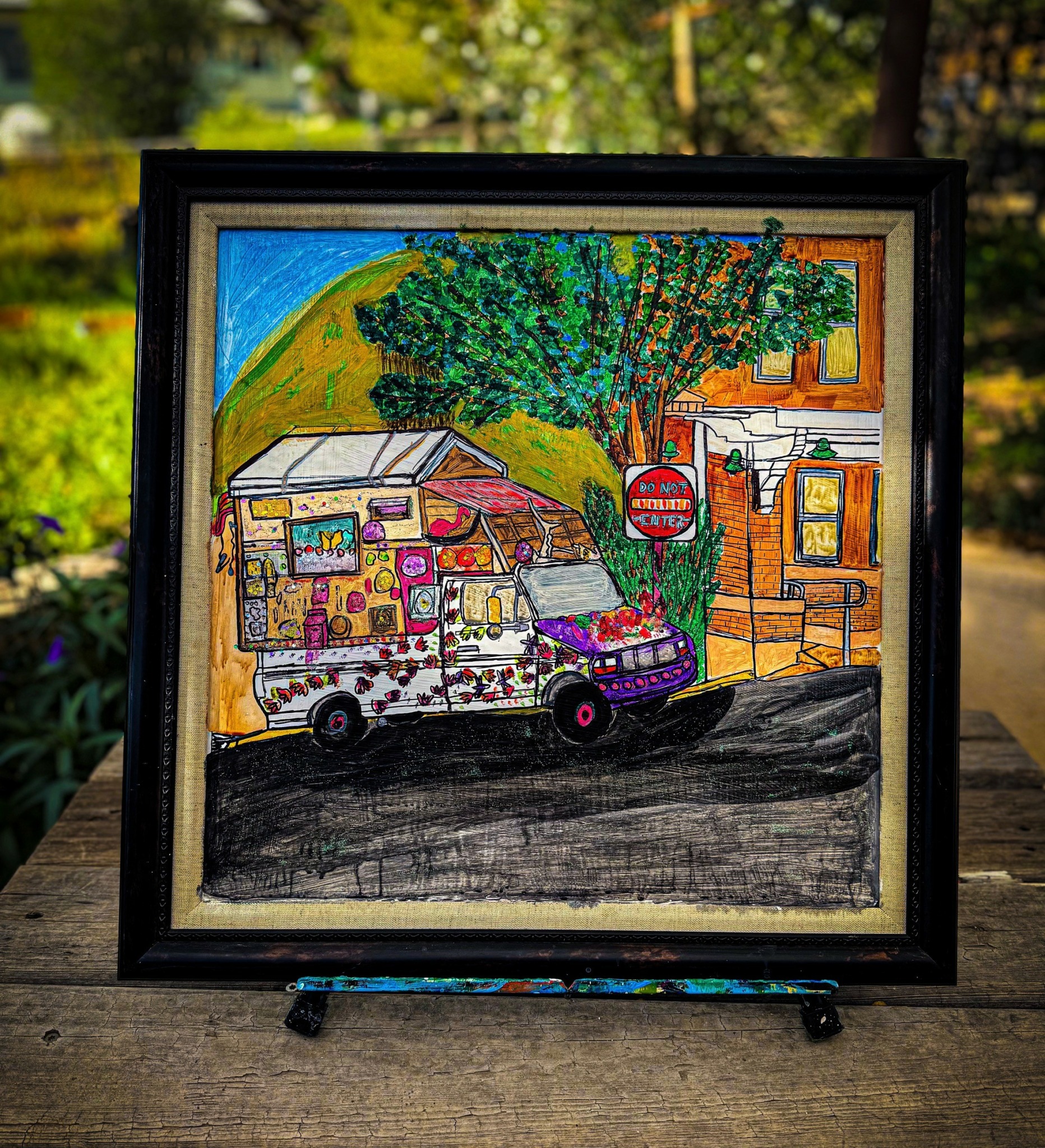 Colorful embroidered scene of a van parked in front of buildings and trees, with a stop sign nearby, on a sunny day.