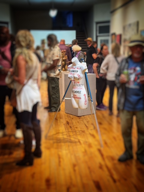 People gather around a table with a white box in a room with wooden floors and artwork on the walls.