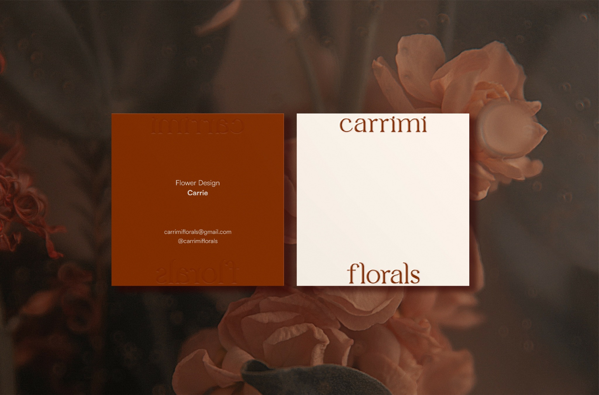 Two business cards on a dark background with pink flowers, one orange and one white, with text about florals and carrimi.